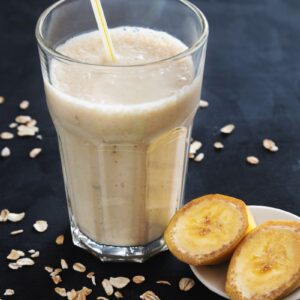 a banana smoothie in a glass next to a plate of sliced bananas