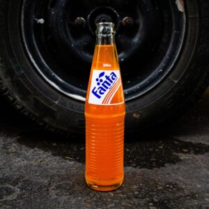 a bottle of soda sitting on the ground next to a tire